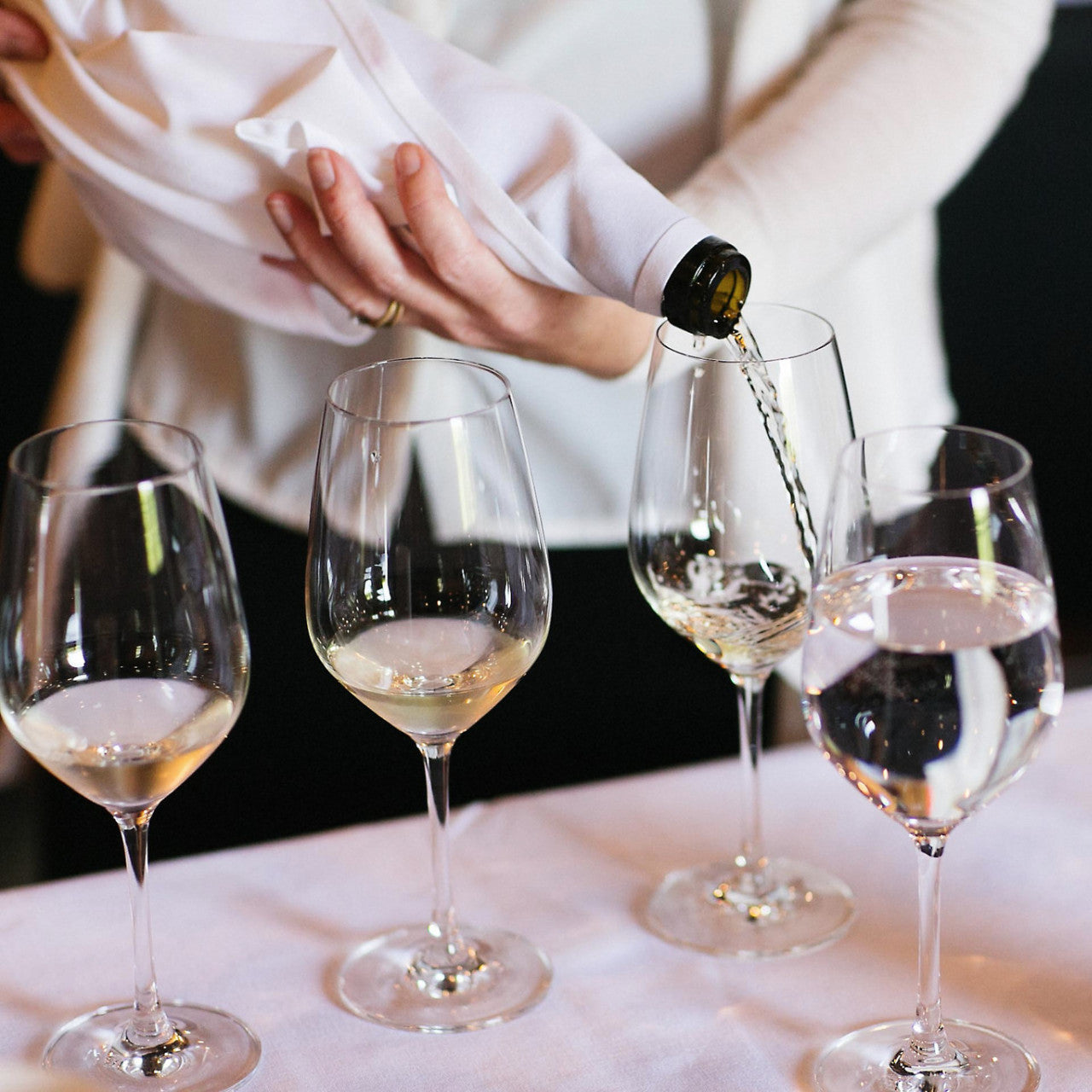 woman holding a wine bottle wrapped in serviette pouring wine into a glass, so the guests don't know what it is