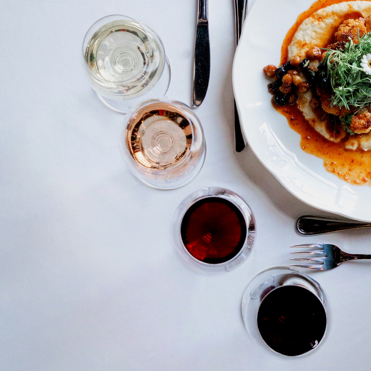 Dinner setting with a plate of food, wine glasses, and small bowls on a white table.